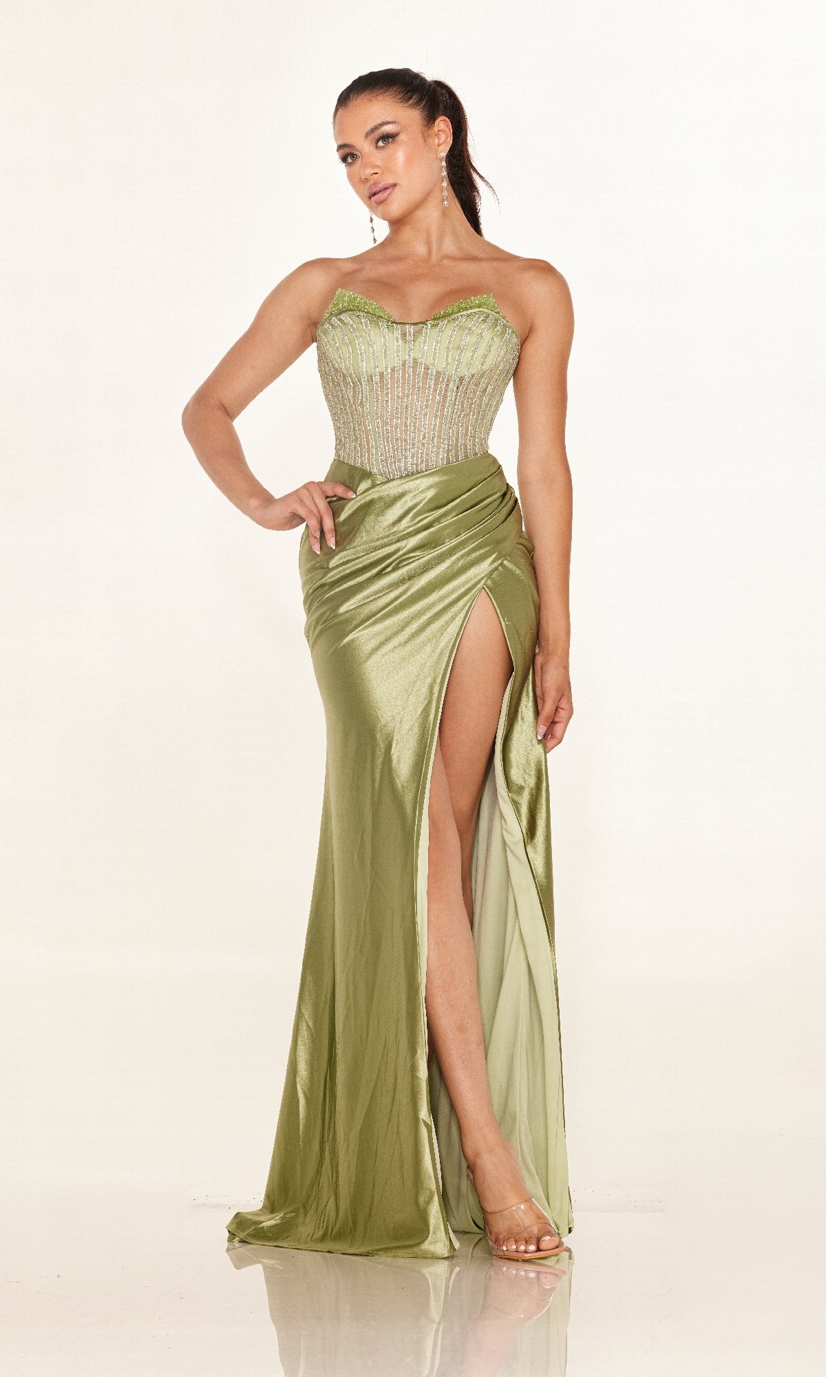 A woman wears the Cecilia Couture 2633 long prom dress, featuring light green satin, an embellished bodice, a high leg slit, and clear high-heeled sandals.